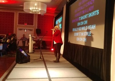 Singer performing karaoke on stage with big screen lyrics and AV crew at Disc Jockeys Unlimited event